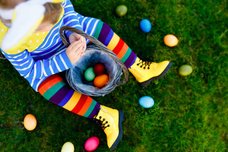 Close-up of legs of toddler girl with colorful stockings and shoes and basket with colored eggs....