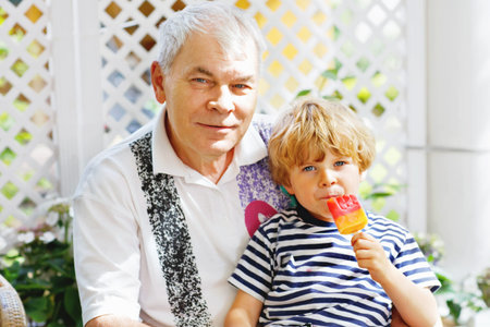 Little blond kid boy and young senior grandfather eating together ice cream in summer