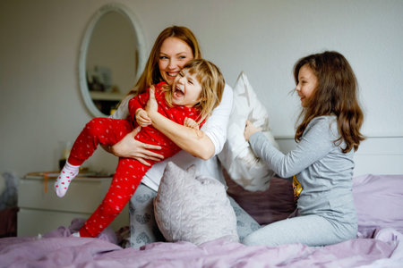 Loving mother and two little sisters girls making pillow fight together. Happy family, woman and...