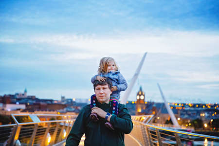 Beautiful portrait of cute little toddler girl with father. Happy baby child hugging with dad. Lovely family of man and daughter. Outdoors at the dusk.の写真素材