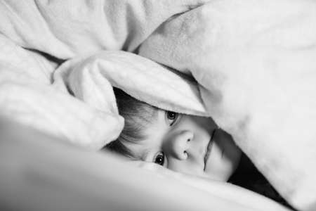Little toddler girl having fun in bed after wake up. Healthy child jump and play hide and seek with parents. Adorable kid at home, family lifestyle.の写真素材