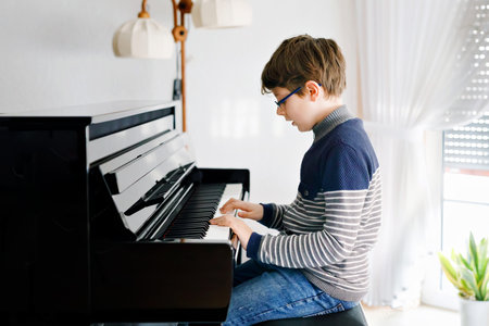 School boy with glasses playing piano in living room. Child having fun with learning to play music instrument. Talented kid during homeschooling virus lockdown.の写真素材