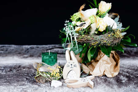Decoration for Easter holiday or spring with soft flower arrangement, green candle and wooden bunnies and eggs.の写真素材