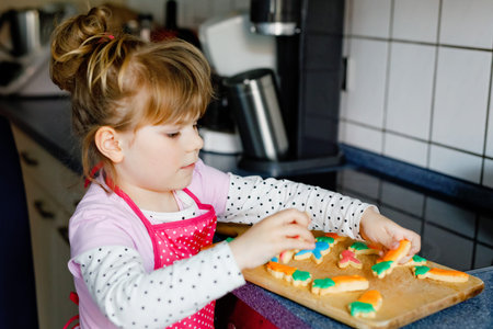 Cute little toddler girl and fresh baked homemade Easter or spring cookies at home indoors. Adorable...