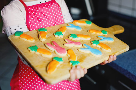 Closeup of cute little toddler girl holding fresh baked homemade Easter or spring cookies at home...