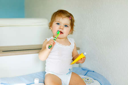 Little baby girl holding toothbrush and brushing first teeth. Toddler learning to clean milk tooth. Prevention, hygiene and healthcare concept. Happy child in bathroomの写真素材