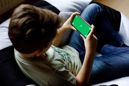 Kid boy gaming or using social media on mobile phone. chroma key compositing the hands of Internet. Child holding smartphone with green screen for commerce, new app and internet. With tracking pointsの写真素材