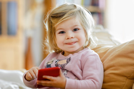 Cute little toddler girl playing with smartphone at home. Healthy baby touching phone with fingers, looking cartoons and having fun with educational games . Early development conceptの写真素材