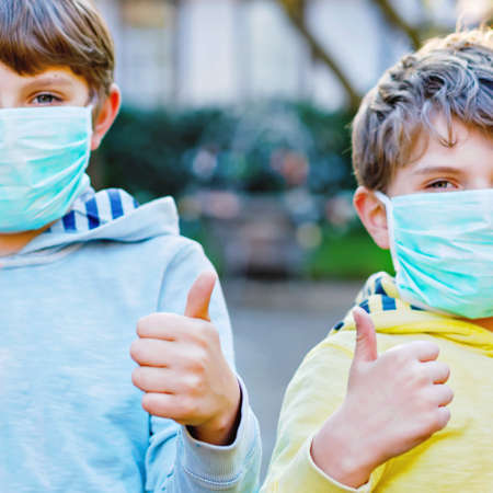 Two kids boys in medical mask as protection against pandemic disease. Children, lovely siblings and best friends using protective equipment as fight .の写真素材
