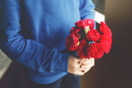 Closeup of hands of preteen kid boy holding bunch of clove flowers. Child congrats and presents cloves to mother or girl friend for mothers day or valentines day.の写真素材