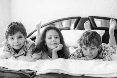 Three happy kids in pajamas celebrating pajama party. Preschool and school boys and girl in nightwear having fun together. Children playing together in bed. Old black and white picture.の写真素材