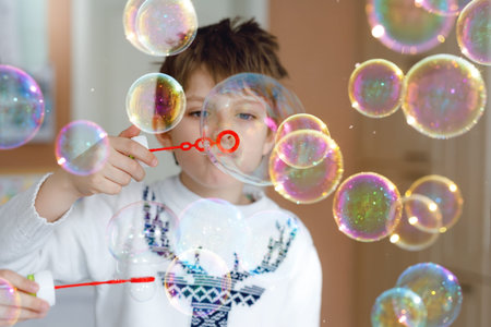 Happy little school boy playing with soap bubbles at home. Kid having fun. Child playing at school,...