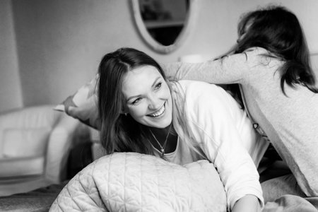 Loving mother and school kid girl making pillow fight together. Happy family, woman and cute...