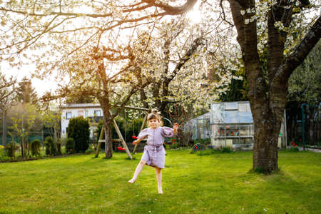 Happy little toddler girl having fun with playing in domestic garden. Smiling positive healthy child run and jump on backyard . Preschool girl laughing and crying. Active leisure and activity outdoorsの写真素材