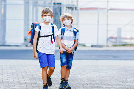 Two kids boys wearing medical mask on the way to school. Children with satchels. Schoolkids on warm sunny day. Lockdown and quarantine time during pandemic diseaseの写真素材