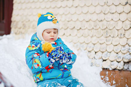 Cute little preschool boy in colorful winter clothes playing with snow and snowflakes, outdoors during snowfall. Active outdoors leisure with children in winter. Happy kid sliding on home stairwayの写真素材
