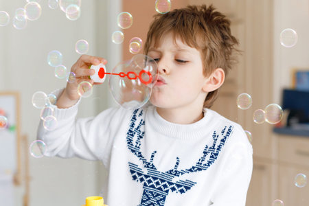 Happy little school boy playing with soap bubbles at home. Kid having fun.