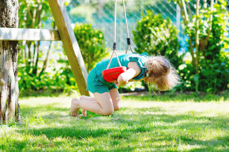 Happy little preschool girl having fun on swing in domestic garden. Healthy toddler child swinging on sunny summer day. Children activity outdoor, active smiling kid laughingの写真素材