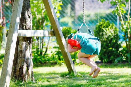 Happy little preschool girl having fun on swing in domestic garden. Healthy toddler child swinging on sunny summer day. Children activity outdoor, active smiling kid laughingの写真素材