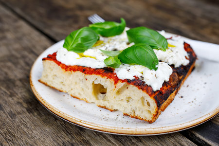 Fresh focaccia with tomato, basil and goat cottage cheese on wooden table. Italian food.