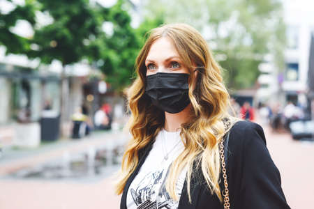 Portrait of young beautiful woman wearing medical mask as protection against corona virus. Covid pandemic time in Europe and in the world. Safety for people. Woman in summer city.の写真素材