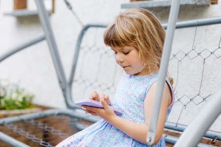 Cute little toddler girl playing with smartphone Healthy baby touching mobile phone with fingers, looking cartoons and having fun with educational apps. Child in garden outdoorsの写真素材