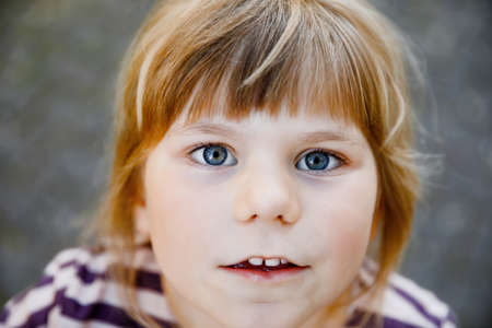 Portrait of happy smiling toddler girl outdoors. Little child with blond hairs looking and smiling at the camera. Happy healthy child enjoy outdoor activity and playing.の写真素材