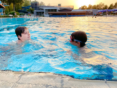 Two school kids boys playing and splashing in an outdoor swimming pool on warm summer day. Happy...