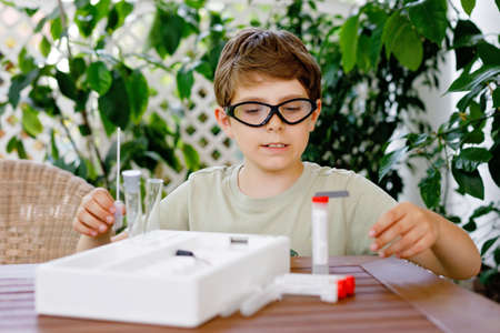 Kid boy doing chemical experiment in laboratory at school. Child with protective glasses study using pipette dropping liquid to test tube , caucasian , biochemistry . chemistry class. Summer school.の写真素材