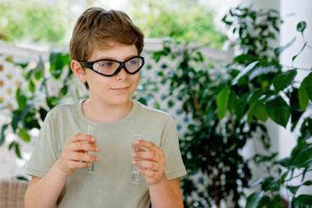 Kid boy doing chemical experiment in laboratory at school. Child with protective glasses study using...