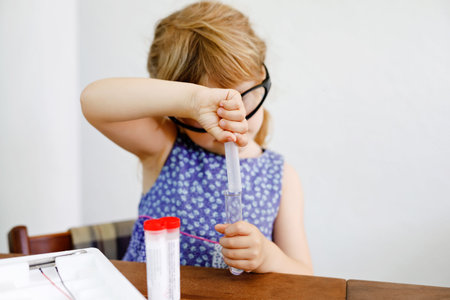 Little preschool girl doing chemical experiment in laboratory at school. Toddler child with...
