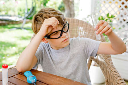 Kid boy doing chemical experiment in laboratory at school. Child with protective glasses study using pipette dropping liquid to test tube , caucasian , biochemistry . chemistry class. Summer school.の写真素材