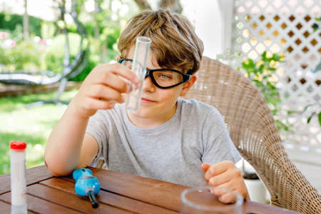 Kid boy doing chemical experiment in laboratory at school. Child with protective glasses study using pipette dropping liquid to test tube , caucasian , biochemistry . chemistry class. Summer school.の写真素材