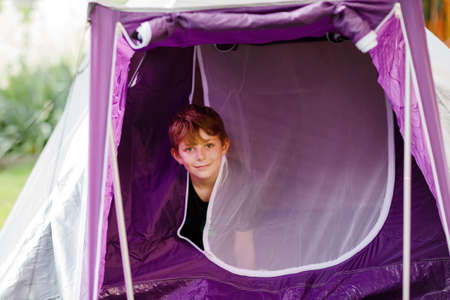 Happy kid boy camping in tent in nature. Healthy school child on hiking vacations in summer. Childr having fun on family or school trip.の写真素材