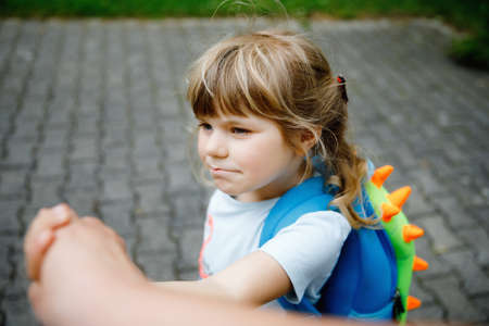 Mother accompanies toddler to kindergarten or daycare. Caring mother holds daughter hand as she goes to school. Upset sad girl. Preschool child does not want to leave mother. fears primary school.の写真素材
