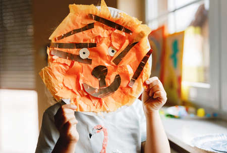 Little preschool girl painting with finger colors making animal tiger craft at home or nursery. Indoor activity with happy creative toddler child, homeschooling with parentsの写真素材