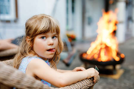 Little toddler girl girl roasting marshmallows on stick at bonfire. Child having fun at camp fire. Camping with children on backyard. Family leisure with kids at summer.の写真素材