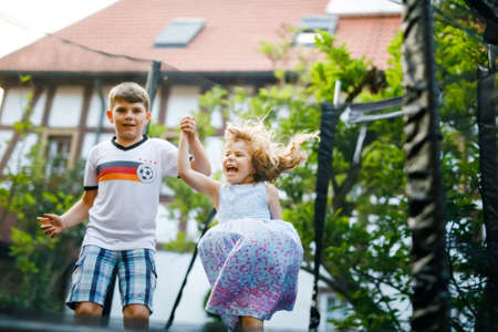 Little preschool girl and school kid boy jumping on trampoline. Happy funny siblings children having fun with outdoor activity in summer. Sports and exercises for kids. Family have fun.の写真素材