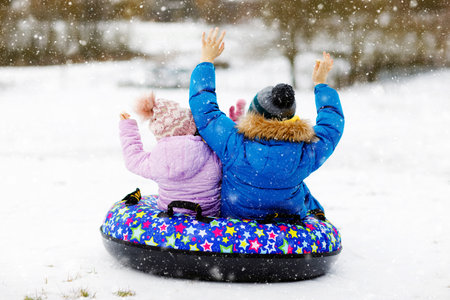 Active toddler girl and school boy sliding together down the hill on snow tube. Children, siblings having fun outdoors in winter on sledge. Brother and sister tubing. No face, unrecognizable personの写真素材