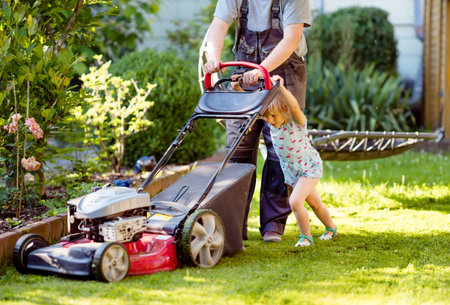 Happy little toddler girl and middle-aged father with lawn mower. Family, daughter, preschool child...