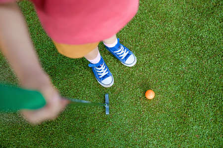 Cute preschool girl playing mini golf with family. Happy toddler child having fun with outdoor activity. Summer sport for children and adults, outdoors. Family vacations or resort.の写真素材