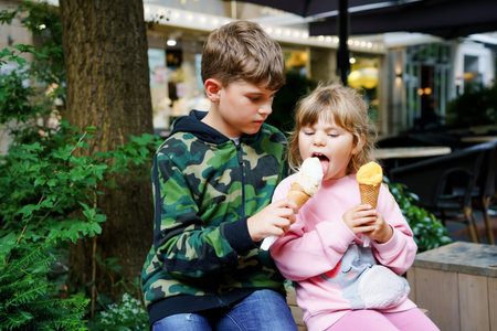 Little preschool girl and school kid boy eating ice cream in waffle cone Happy children, brother and sister eat icecream dessert. Family in the city. Siblings in love.の写真素材
