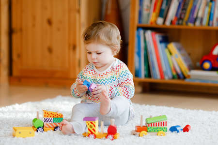 little baby girl playing with educational wooden toys at home or nursery. Toddler with colorful train. Child having fun with different toys. Lonely kid during virus pandemic quarantineの写真素材