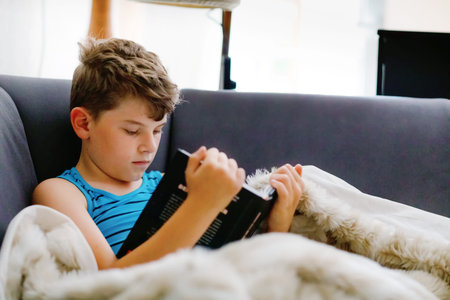 Cute blond little kid boy reading magazine or book in domestic room. Excited child reading loud,...