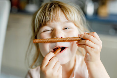 Portrait of happy little preschool girl holding chocolate waffle rolls. Smiling hungry toddler child with sweet biscuit wafer. Sweet sugar cocoa waffles.の写真素材