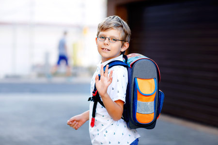 Happy little kid boy with glasses and backpack or satchel. Schoolkid on the way to school. Portrait...