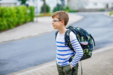 Happy little kid boy with satchel and eyeglasses. Schoolkid wearing glasses on the way to middle or high school. Excited child outdoors on school yard. Back to school.の写真素材