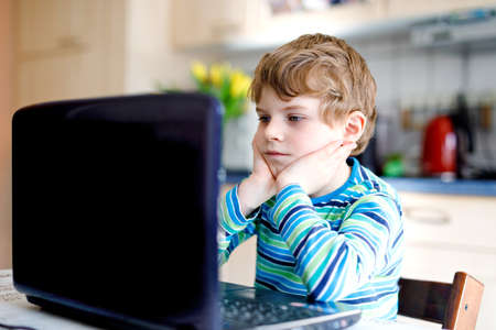 Kid boy learning at home on laptop for school. Elementary school child making homework and using notebook and modern gadgets. Home schooling concept. Having a video lesson with teacher.の写真素材