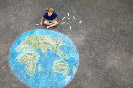 Little preschool girl with earth globe painting with colorful chalks on ground. Positive toddler...