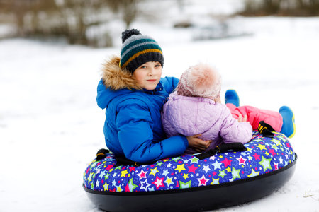 Active toddler girl and school boy sliding together down the hill on snow tube. Happy children,...